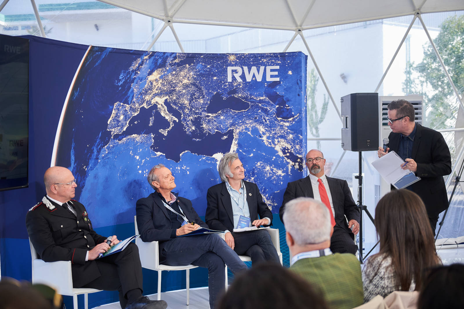 Una discussione di panel con cinque persone davanti a uno sfondo che presenta un'immagine satellitare dell'Europa.