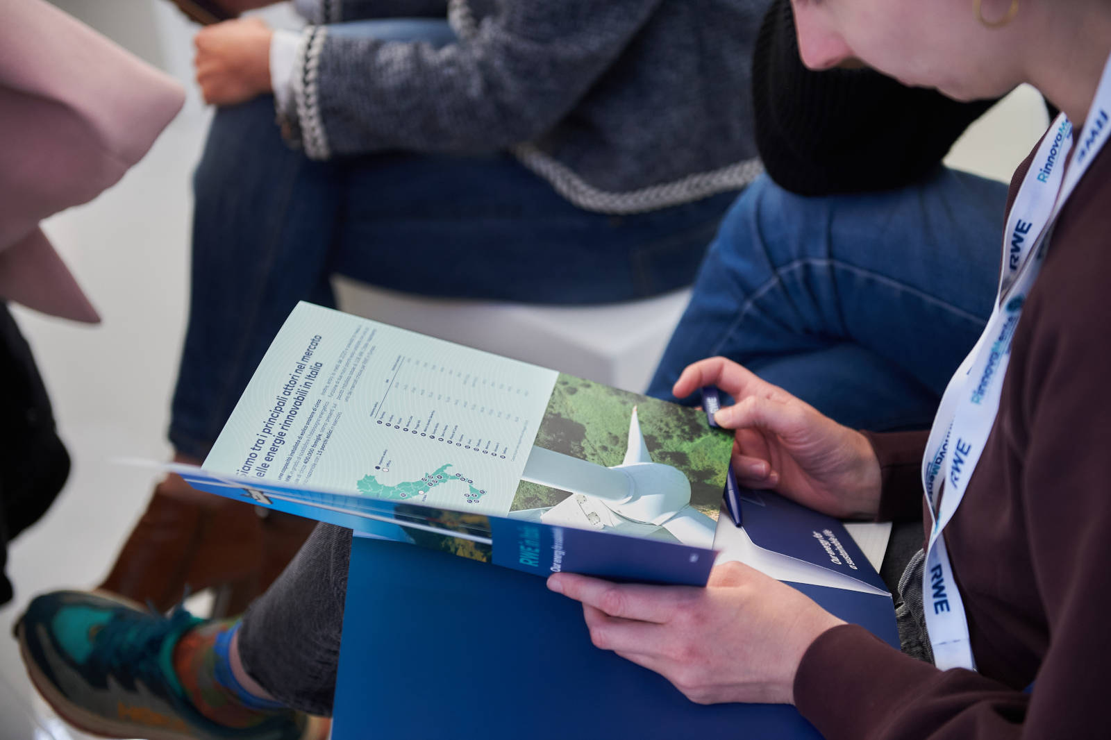 Una persona esamina un opuscolo sull'energia eolica, con una turbina eolica e una mappa, durante un evento.