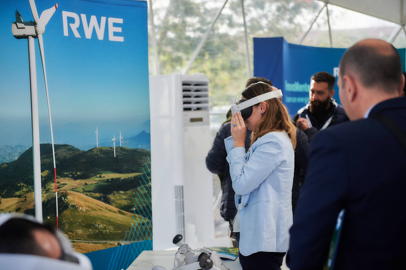 Una donna interagisce con attrezzature di realtà virtuale a un evento che mostra energie rinnovabili e turbine eoliche.