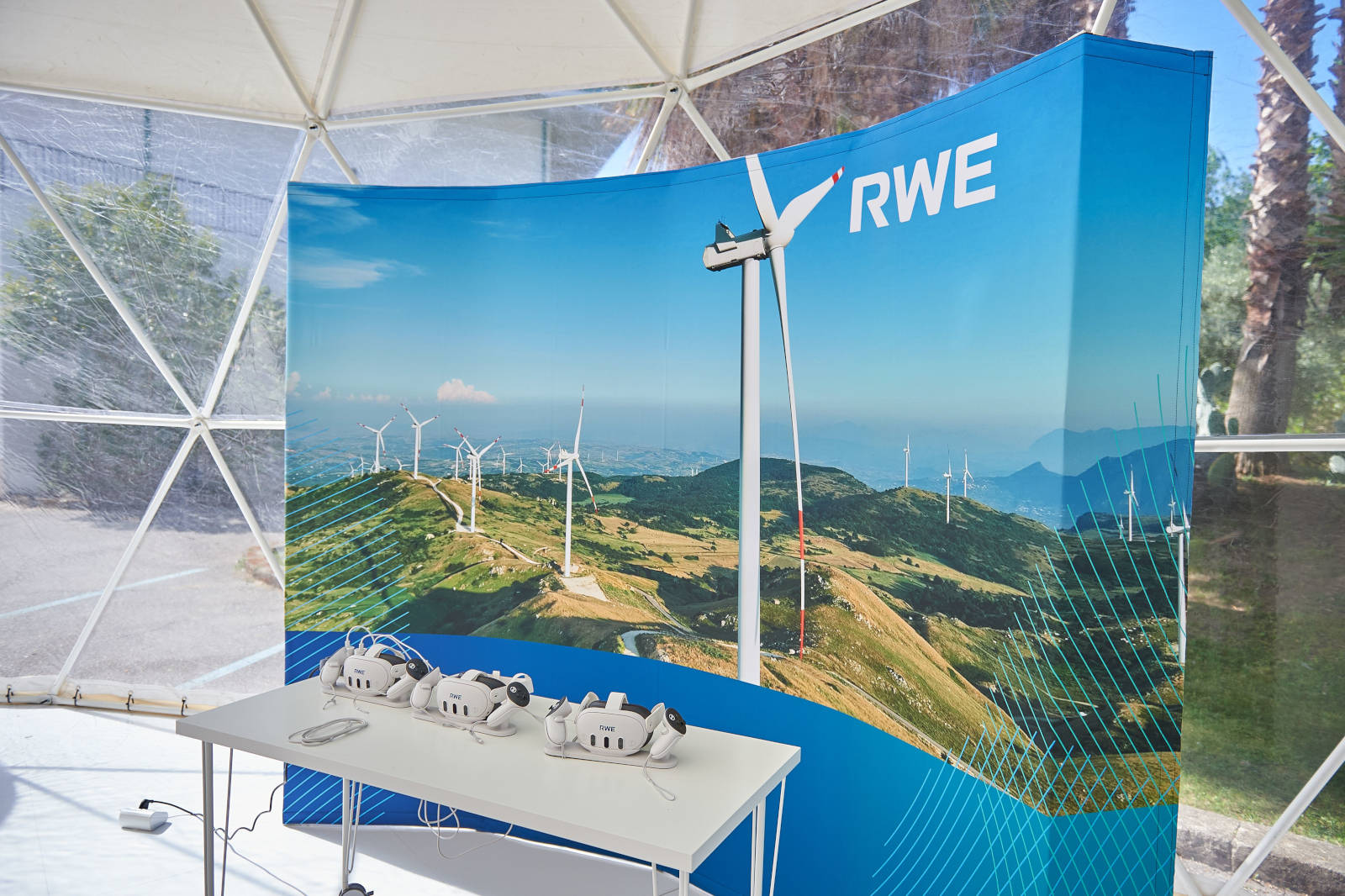 Uno spazio espositivo con uno sfondo di turbine eoliche e un tavolo con visori per la realtà virtuale.