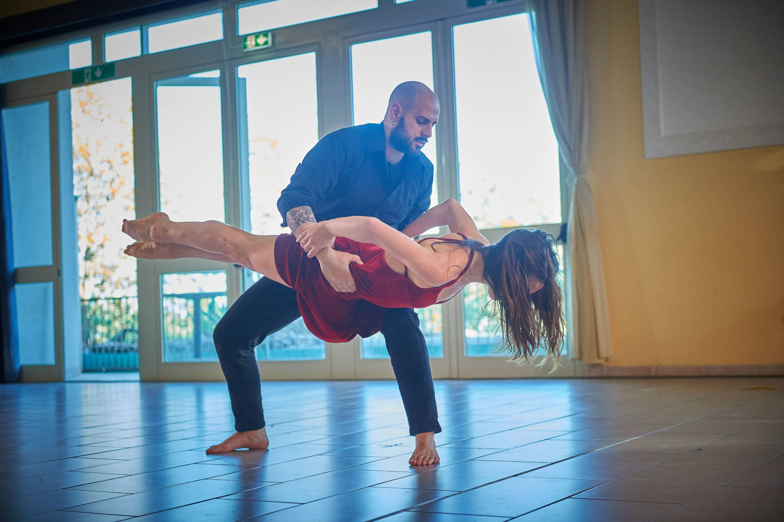 Una coppia balla in uno spazio aperto, con una donna in abito rosso sollevata da un uomo in camicia nera.