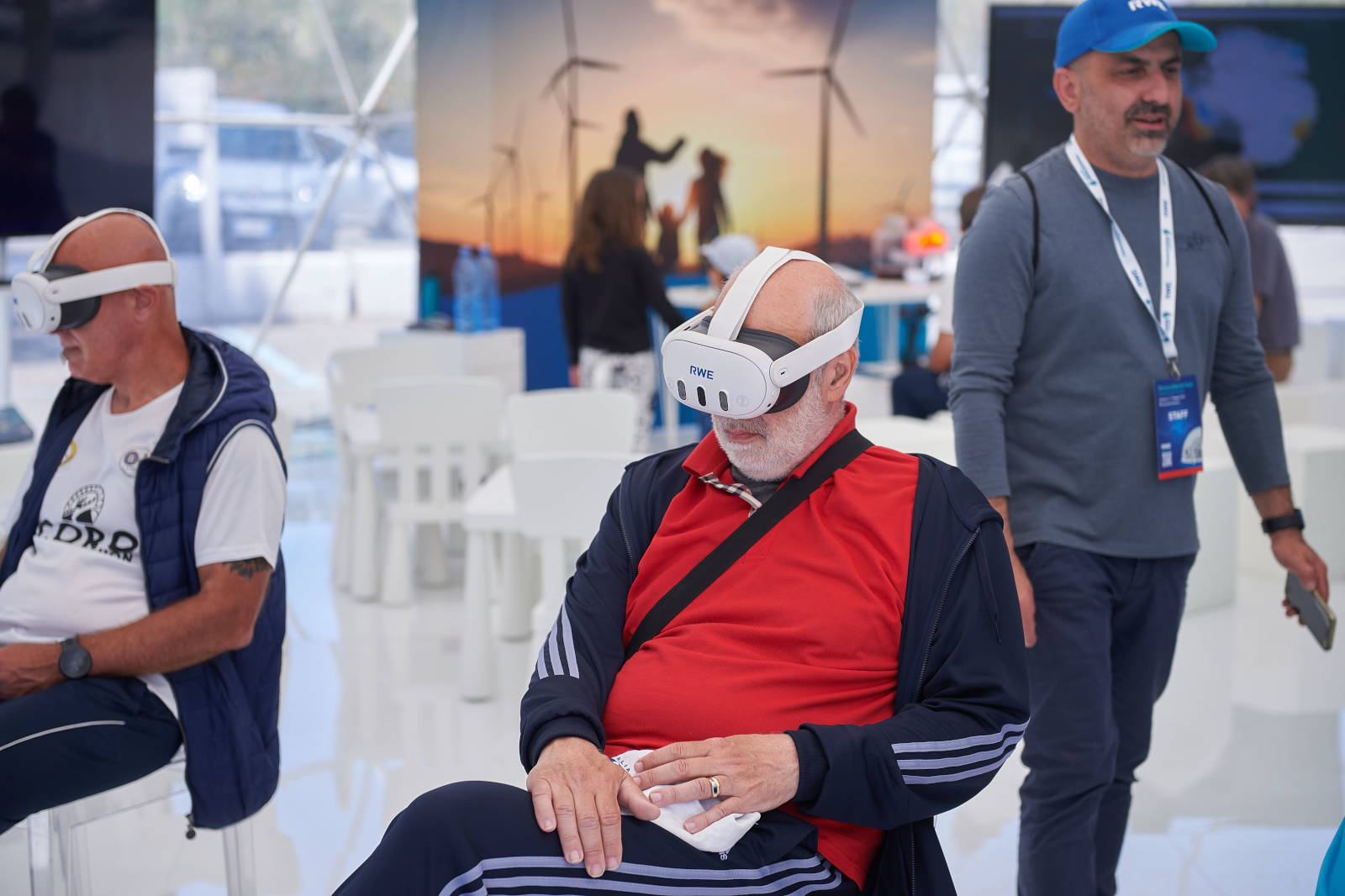 Persone che partecipano a un'esperienza di realtà virtuale a un evento, con turbine eoliche sullo sfondo.