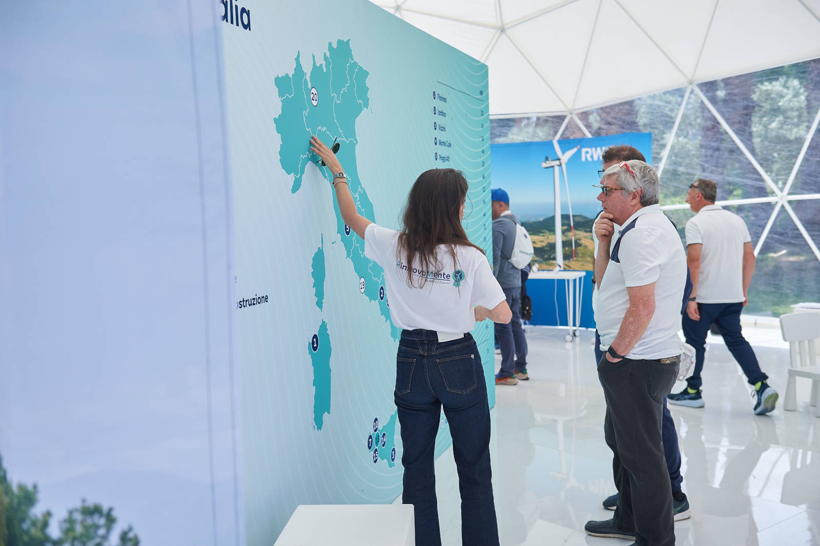 Una persona indica una mappa dell'Italia in una manifestazione, con partecipanti nel background che osservano.