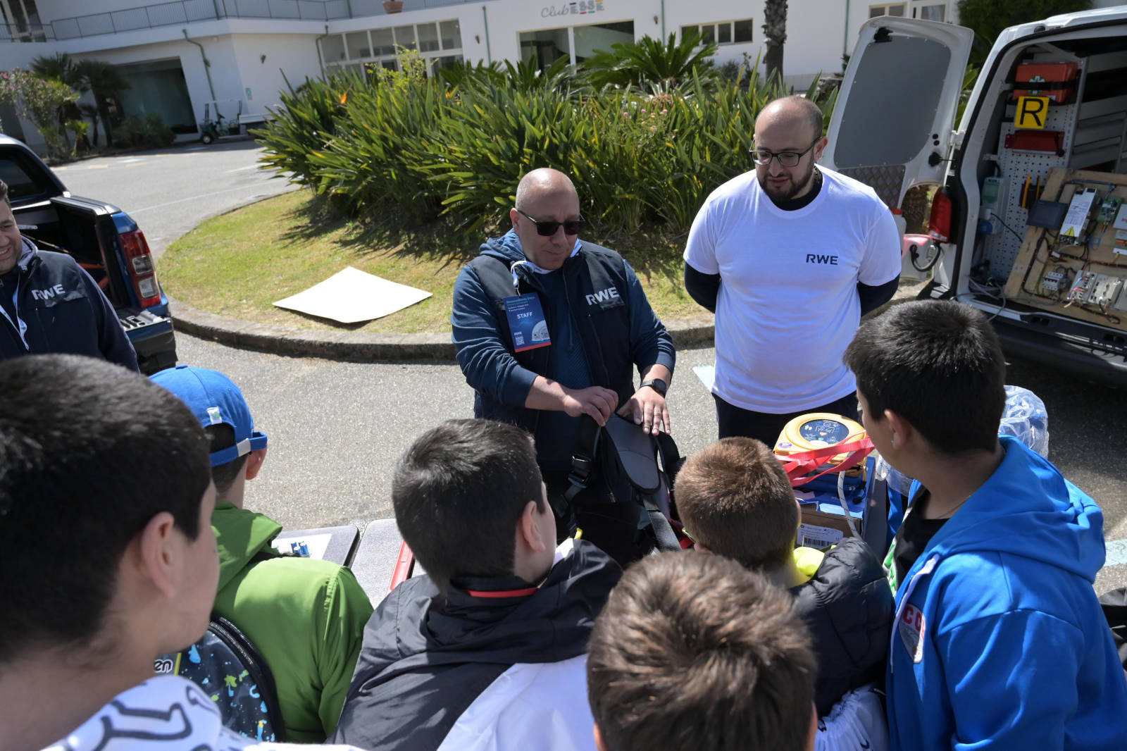 Un piccolo gruppo di bambini ascolta attentamente due adulti che dimostrano attrezzature all'aperto.