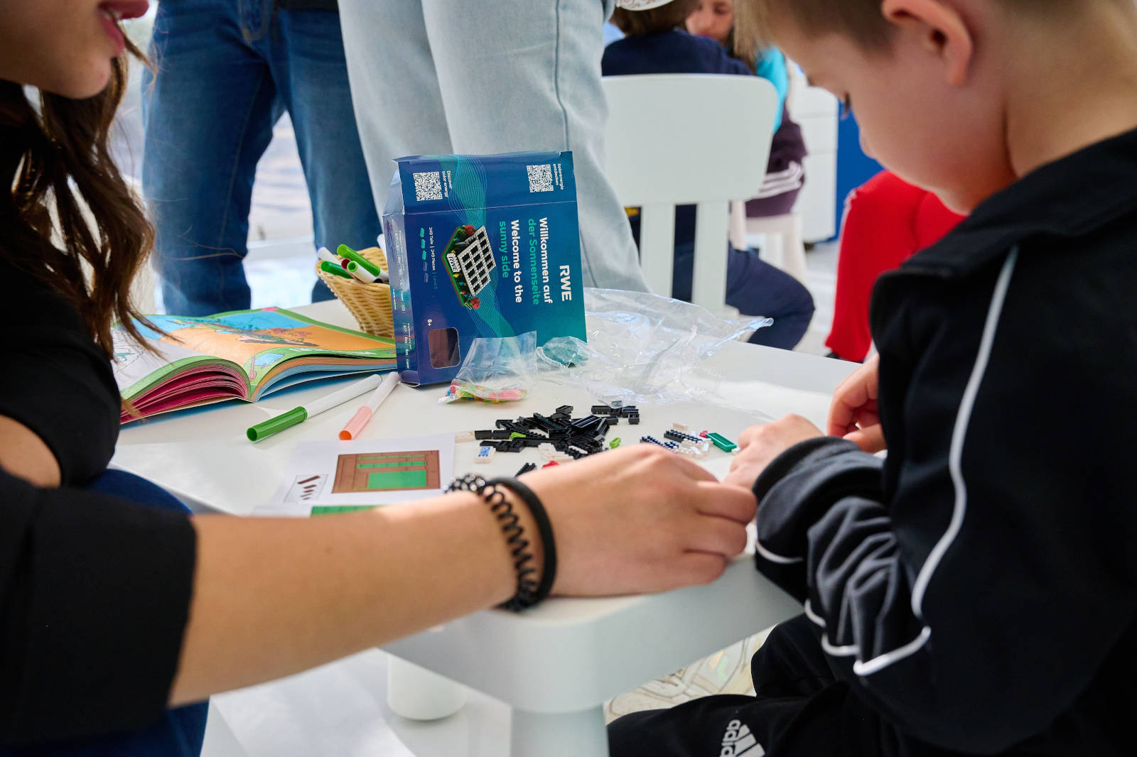 Un bambino e un adulto si dedicano al gioco creativo con mattoncini ed evidenziatori su un tavolo, accompagnati da un libro colorato.