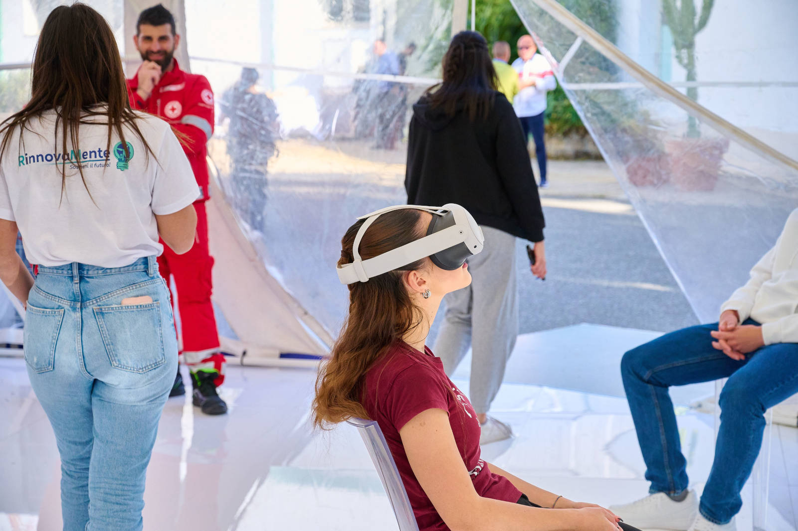 Una donna seduta che indossa un visore VR in uno spazio luminoso con persone che interagiscono sullo sfondo.