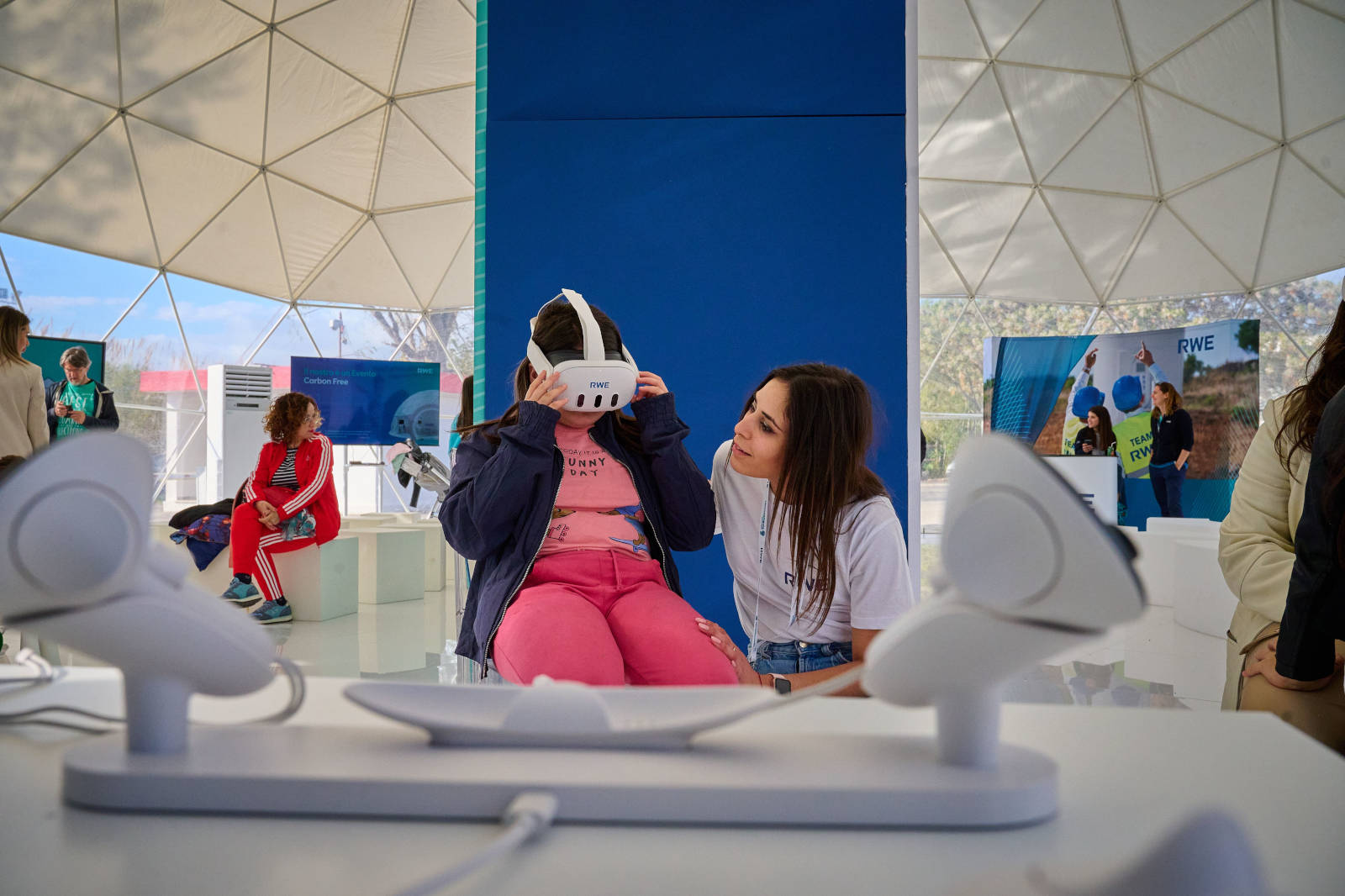 Una ragazza giovane indossa un visore VR mentre un'altra ragazza interagisce con lei in un evento tecnologico dentro un dome geodetico.