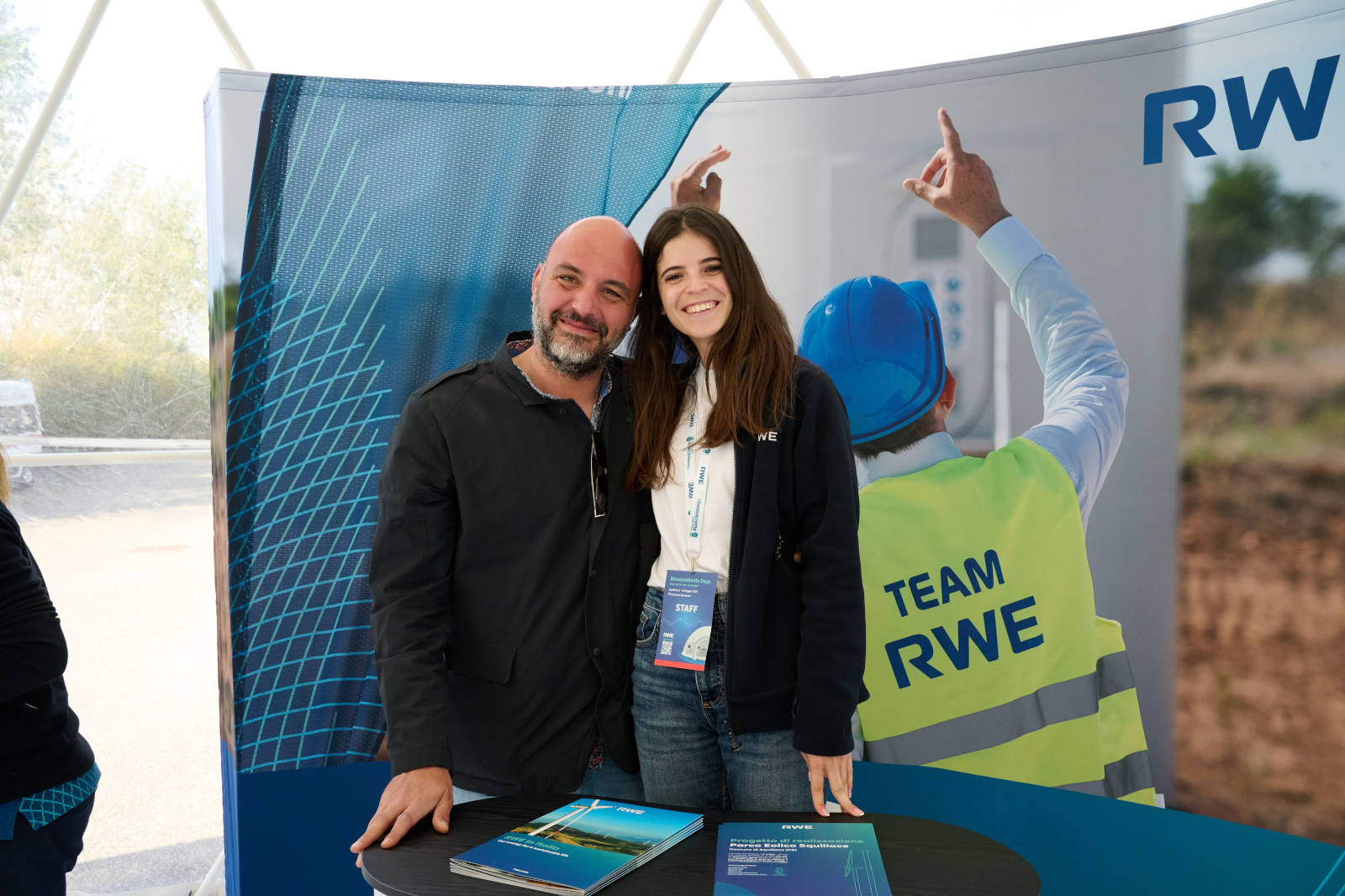 Due persone si trovano davanti a un banner RWE a un evento, con depliant su un tavolo.