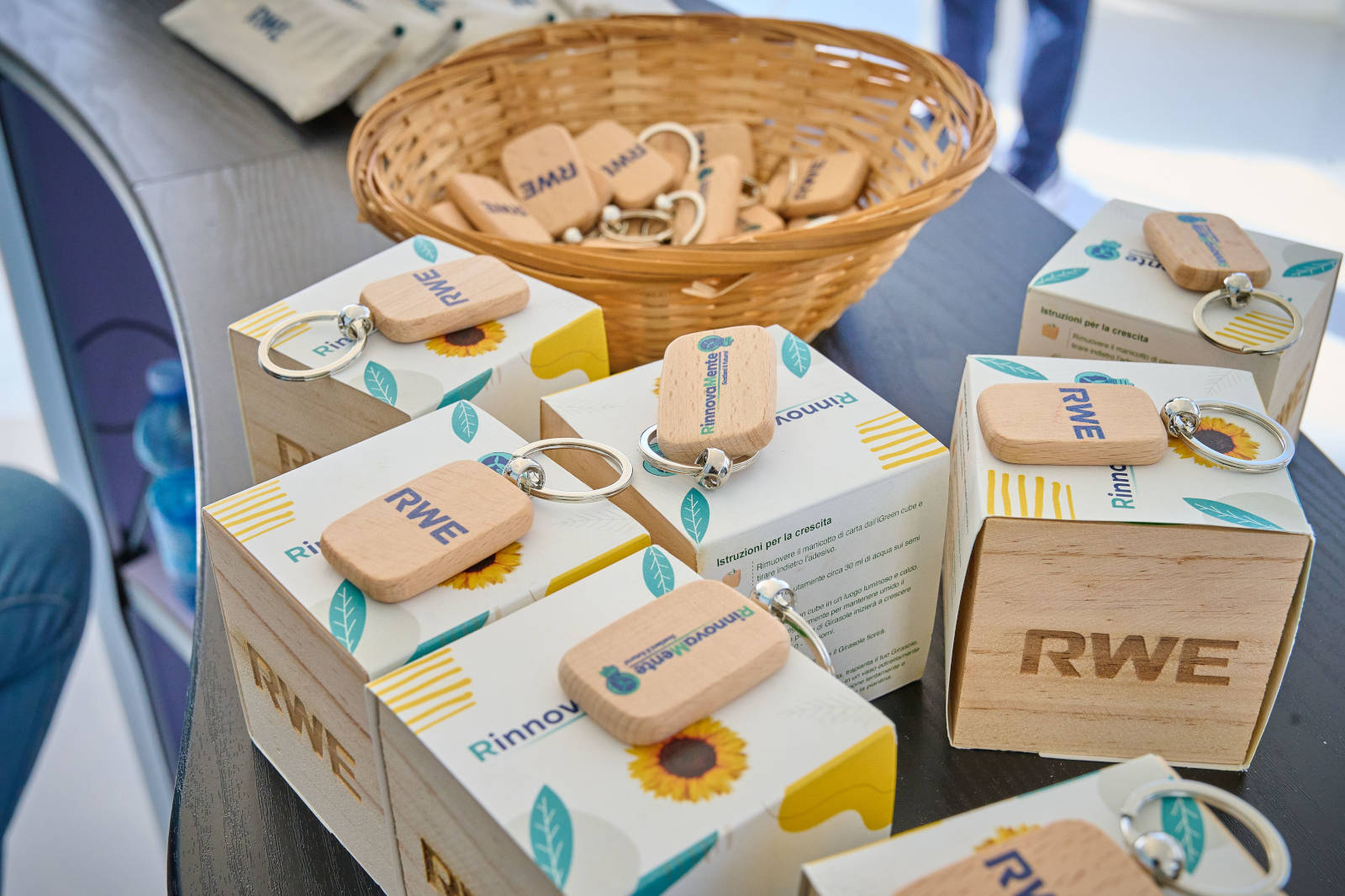 Un'esposizione con portachiavi in legno e scatole colorate etichettate RWE, disposte su un tavolo con un cesto di portachiavi aggiuntivi.
