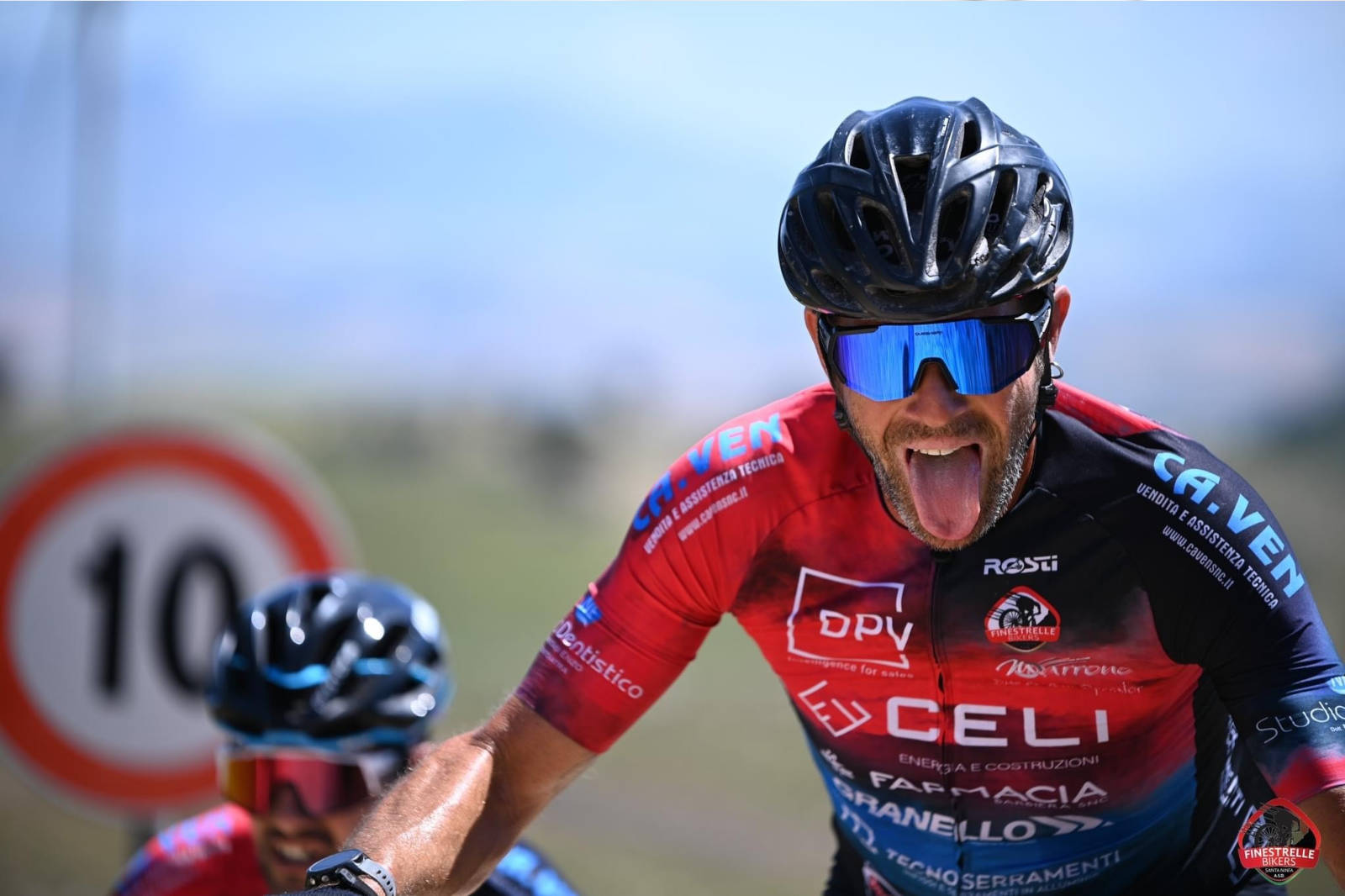 Two cyclists in brightly coloured jerseys near a road sign indicating a speed limit of 10.