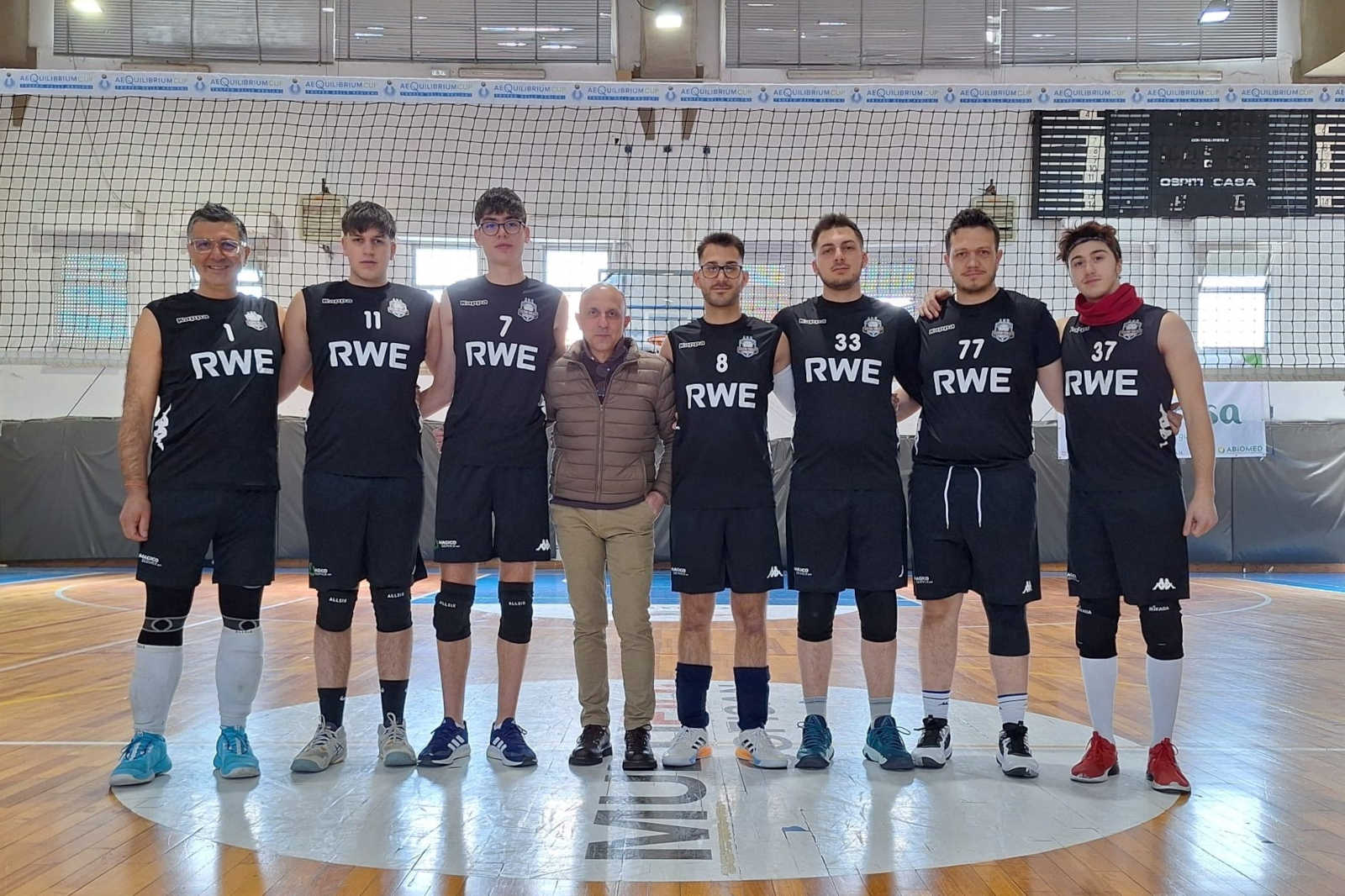 A volleyball team in black uniforms poses together in a gym, showcasing teamwork and athleticism.