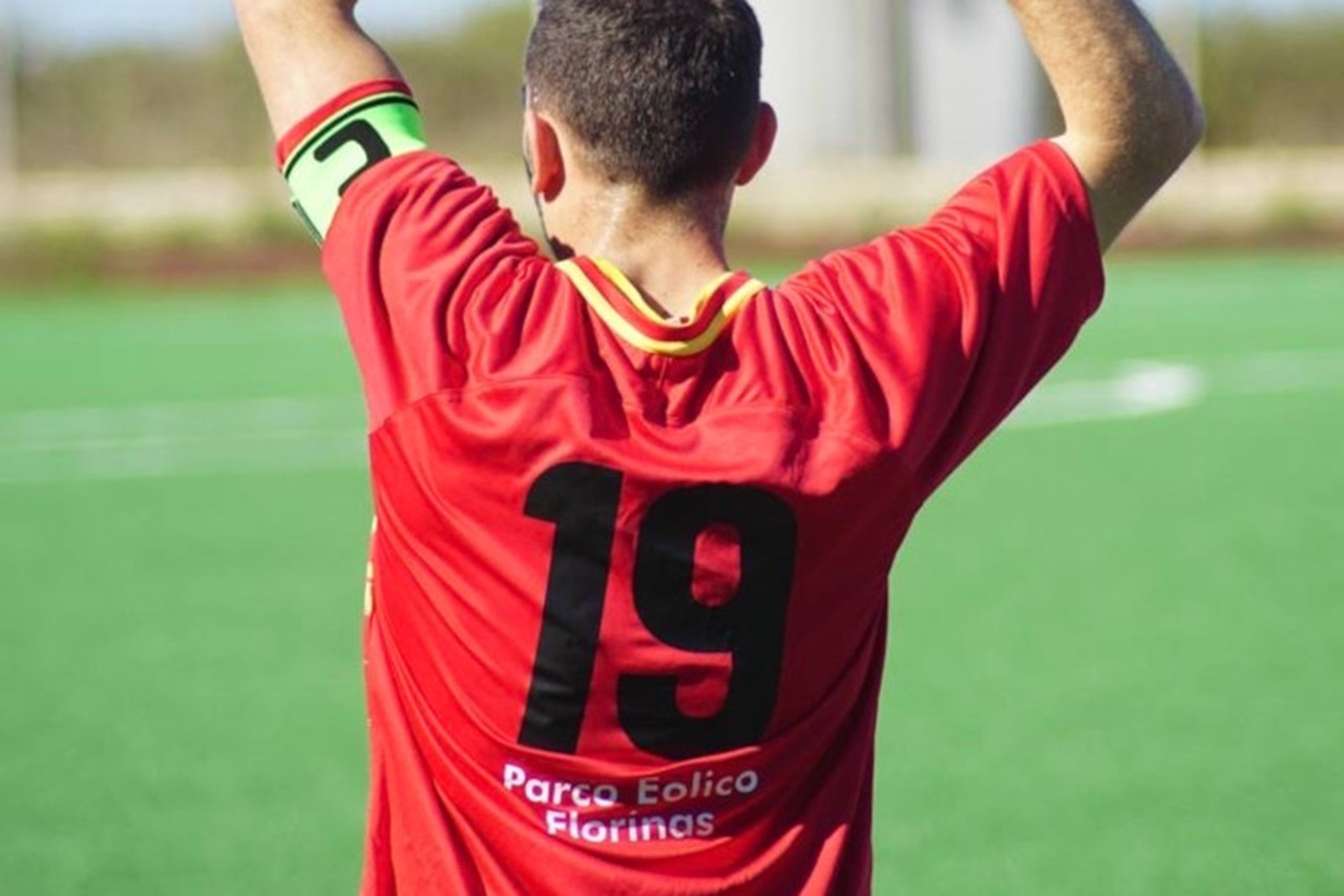 Un giocatore di calcio in maglia rossa si prepara a effettuare un rimessa, indossando una fascia da capitano verde.