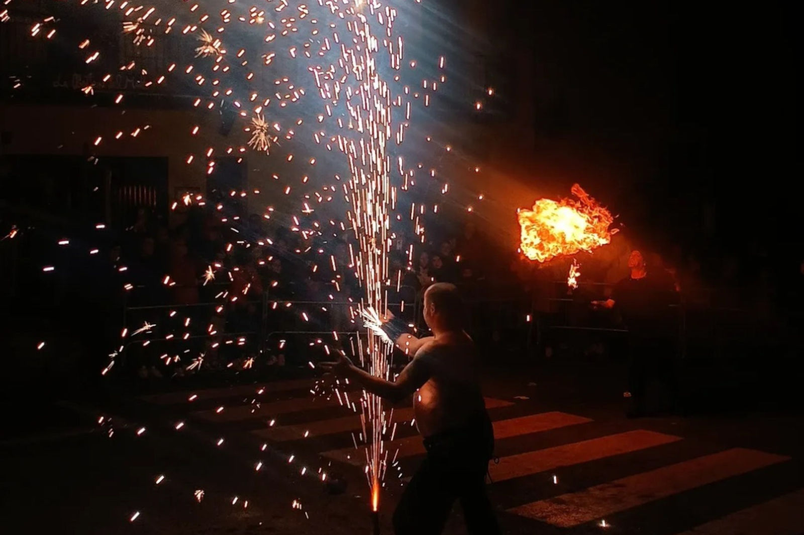 Un performer crea scintille e fuoco durante uno spettacolo notturno, catturando un pubblico con drammatici effetti pirotecnici.