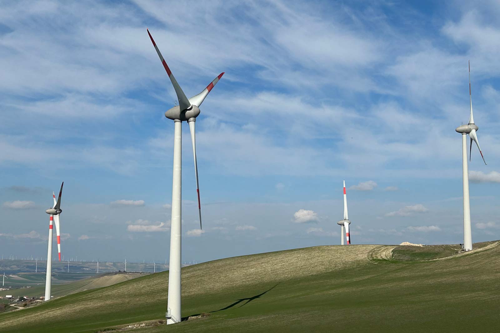 Four wind turbines on green hills under a blue sky with wispy clouds.