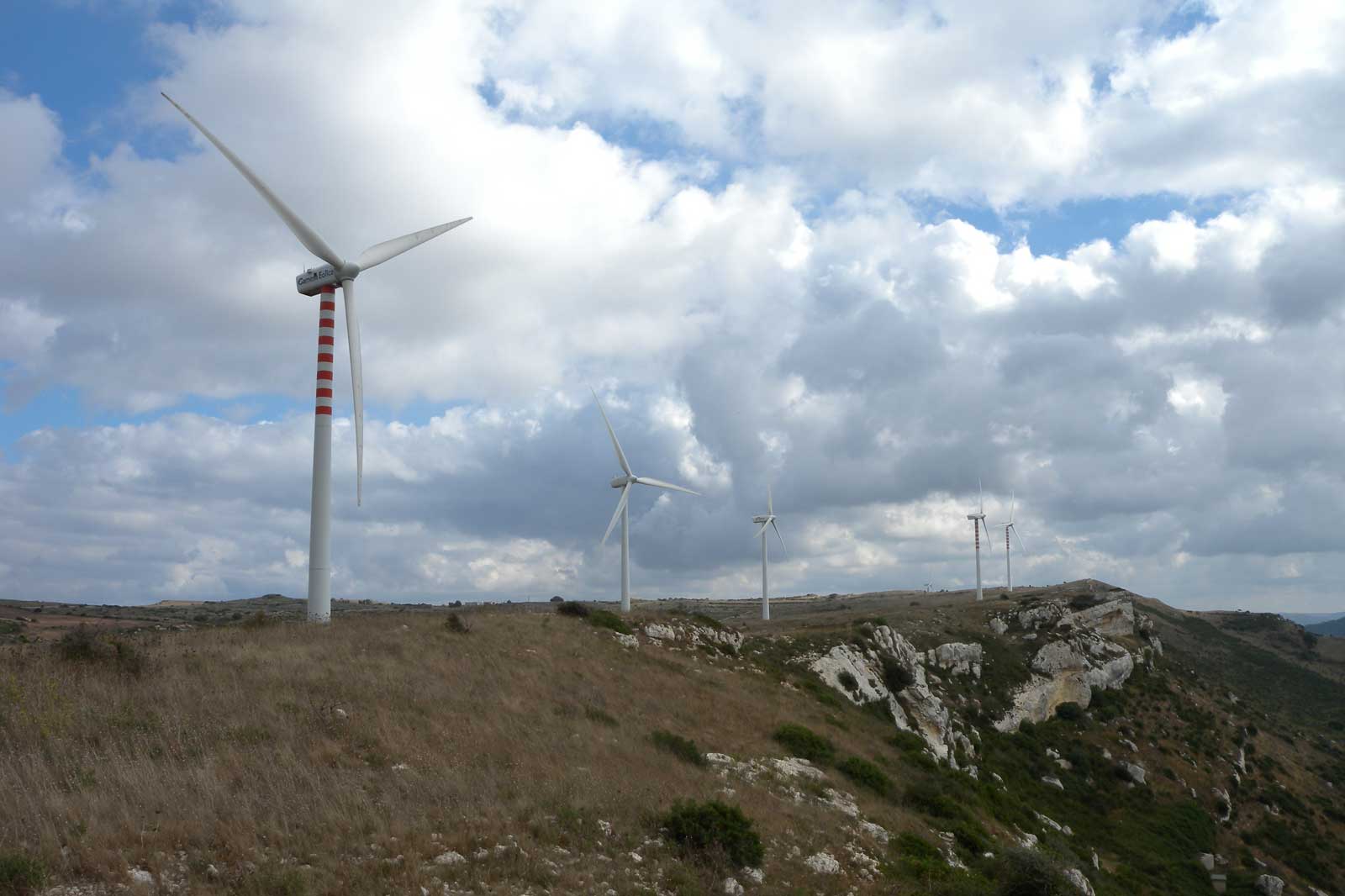A landscape with several wind turbines on a hill, under a cloudy sky with patches of blue.