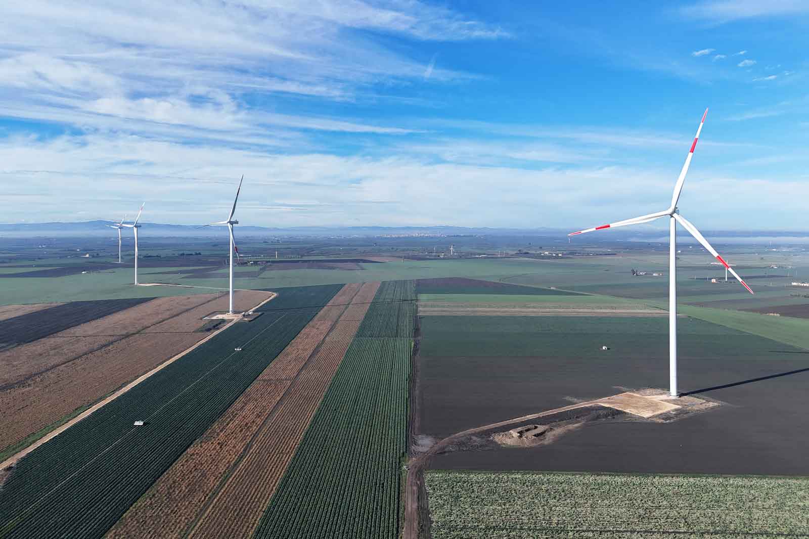 Aerial view of wind turbines on agricultural fields with a clear blue sky in the background.