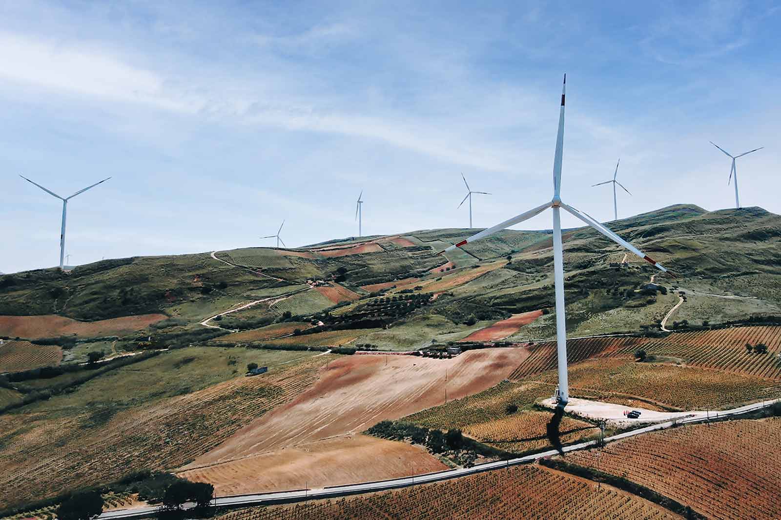 Un paesaggio panoramico con turbine eoliche su colline ondulate, con campi coltivati e un cielo blu chiaro.