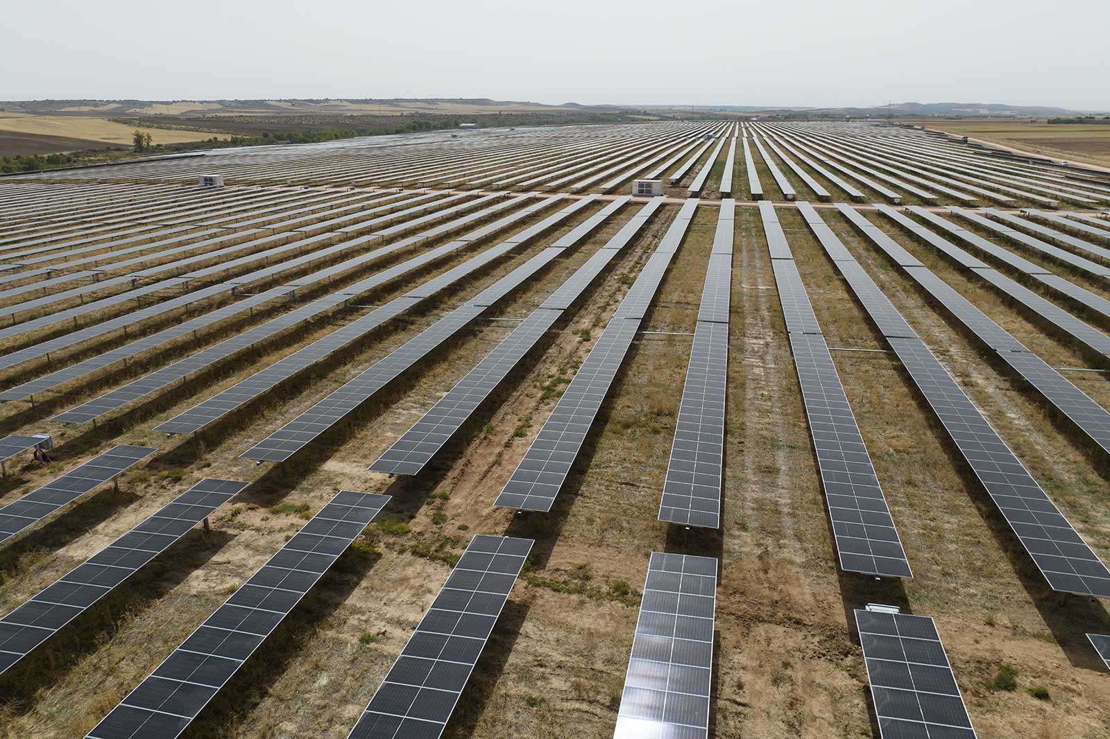 Vista aerea di un grande parco solare con numerosi filari di pannelli solari in un paesaggio secco.