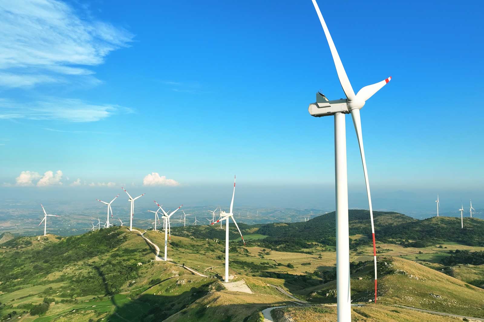 Una vista panoramica di turbine eoliche su colline ondulate sotto un cielo sereno.