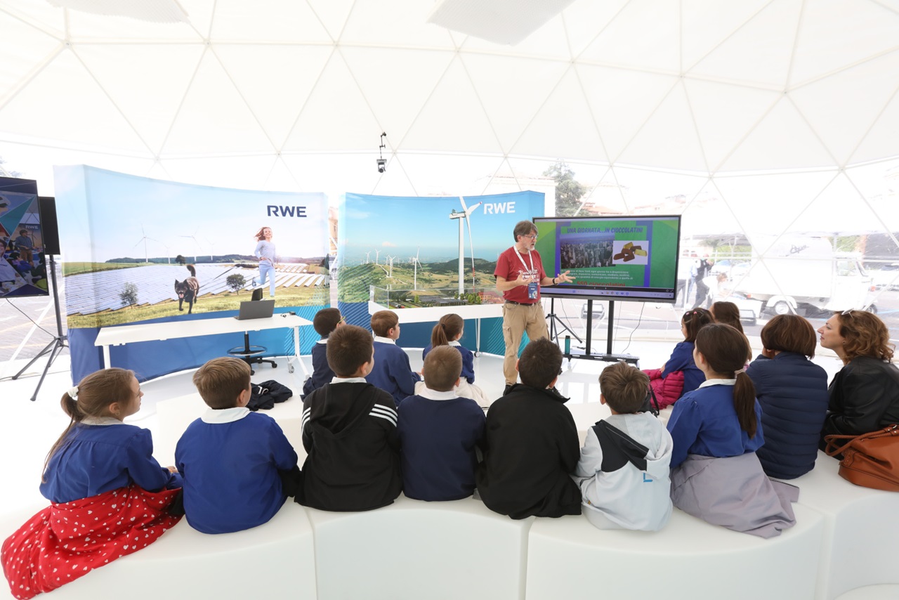 Una presentazione in uno spazio informativo a cupola con bambini seduti, che osservano un relatore che parla di energia rinnovabile.