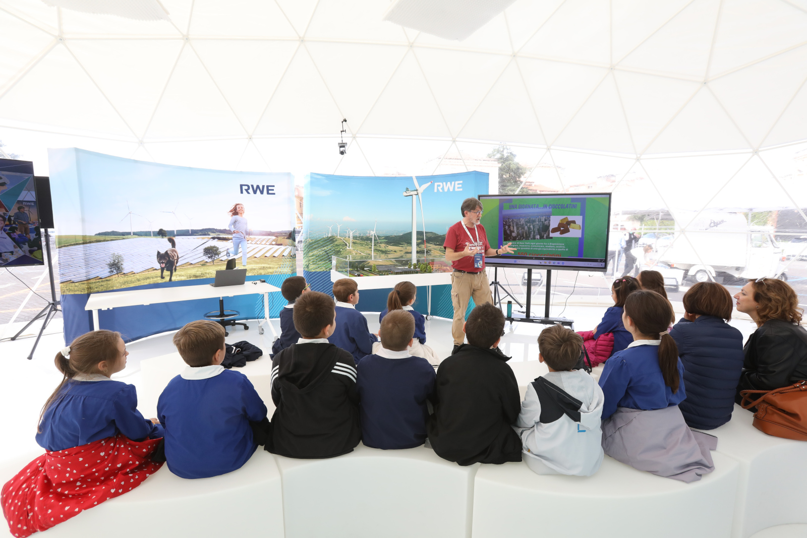 Una presentazione in uno spazio informativo a cupola con bambini seduti, che osservano un relatore che parla di energia rinnovabile.