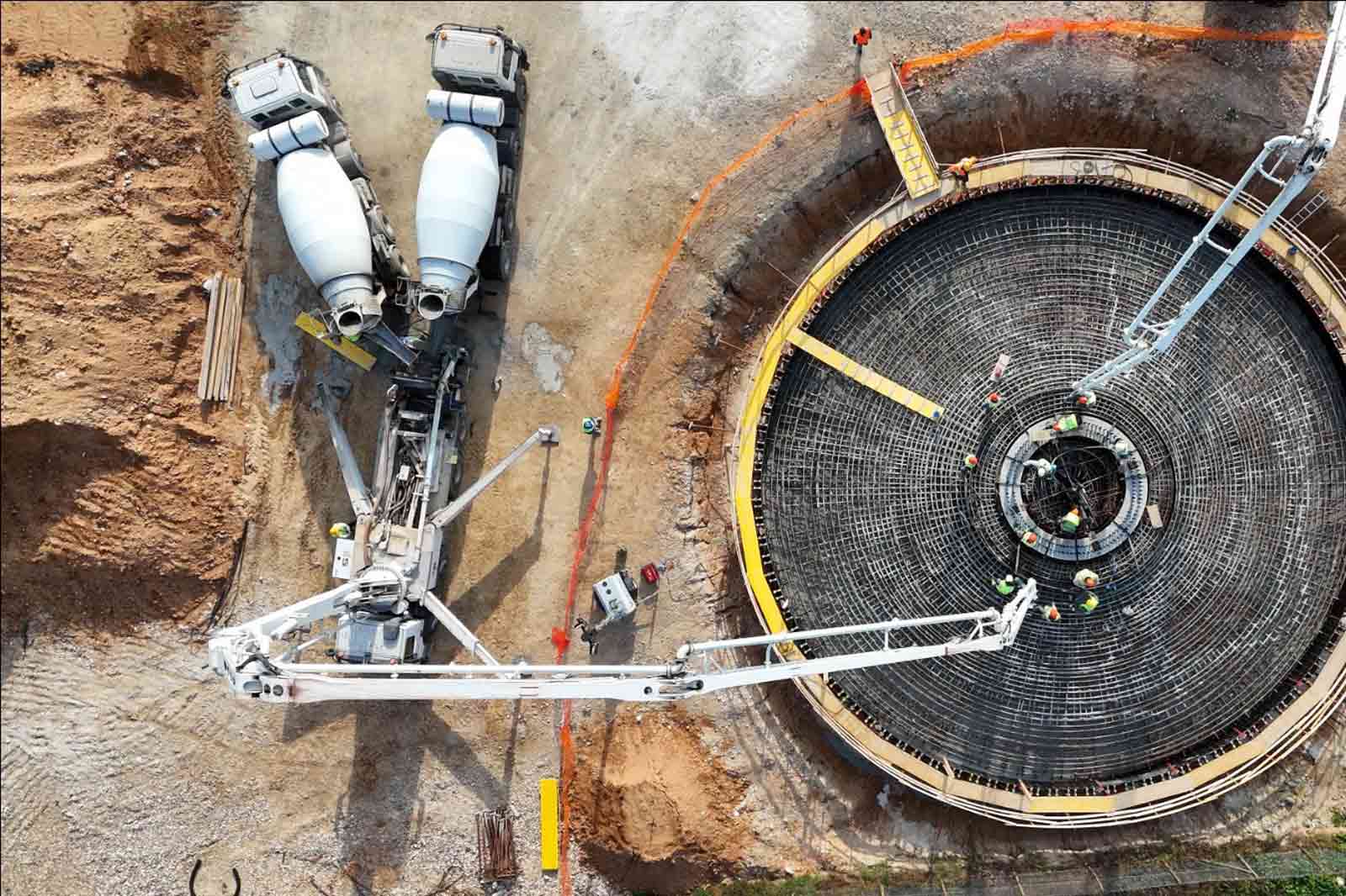 Una vista aerea di un cantiere con due betoniere e operai che preparano una grande fondazione circolare.