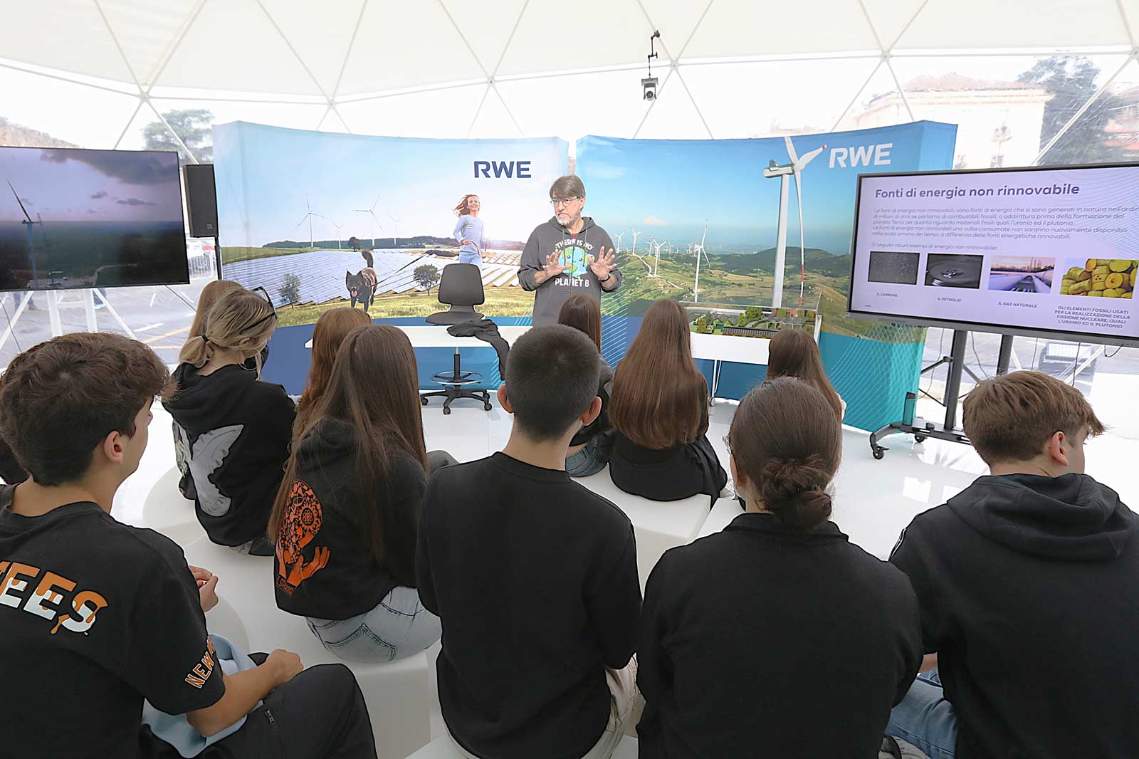 Un gruppo di giovani che osservano una presentazione sull'energia rinnovabile in una struttura a cupola, con pannelli solari e turbine eoliche.